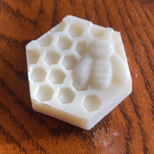 A white honeycomb patterned hexagon soap with a bee shape in relief on the surface.